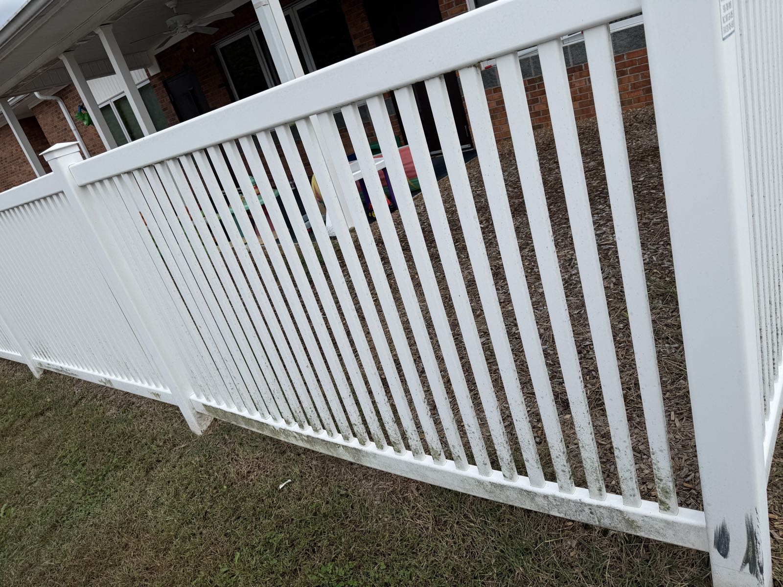 White vinyl daycare fence with green mold and mildew along the bottom rail before soft washing in Greensboro NC